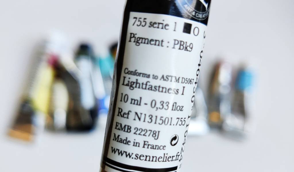 Gros plan sur un tube d'aquarelle (755 serie 1 - carré noir - rond blanc - Pigment : PBk9 - Conforms to ASTM D5067 - Lightfastness I - 10 ml - 0,33 floz Ref N131501.755 - EMB 22278J Made in France www.sennelier.fr