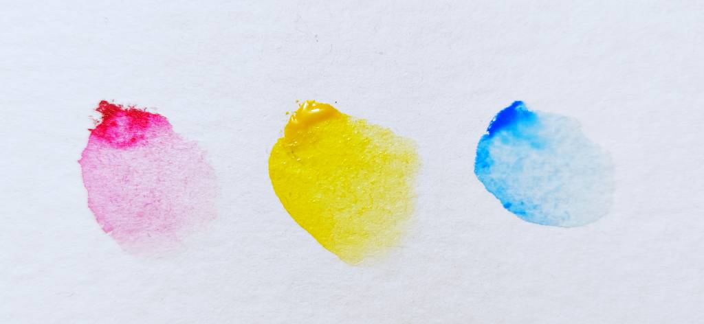 Trois touches de peinture sur papier blanc : un "rouge" (plus proche du rose), un jaune, un bleu