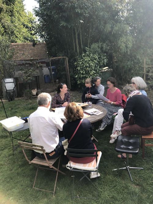 Huit personnes autour d'une table où du matériel est posé, dans un jardin