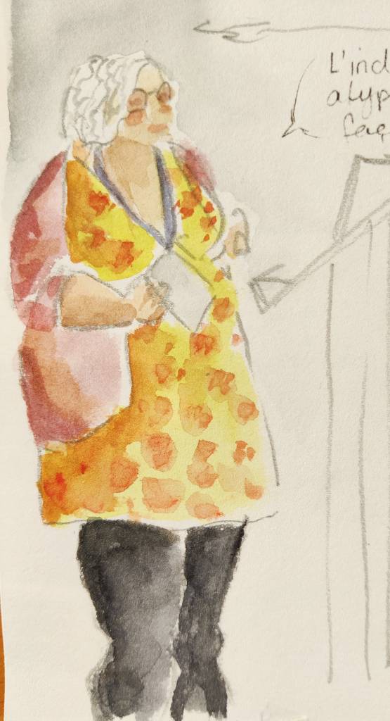 Croquis d'une femme debout en robe jaune à fleurs (sur le croquis, c'est plus des taches). On devine peut-être qu'elle est en train de faire une conférence