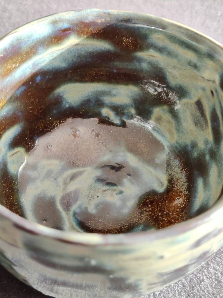 Détail de l'intérieur d'un petit pot en argile recouvert d'émail vert/bleu foncé/miel posé de façon très irrégulière.