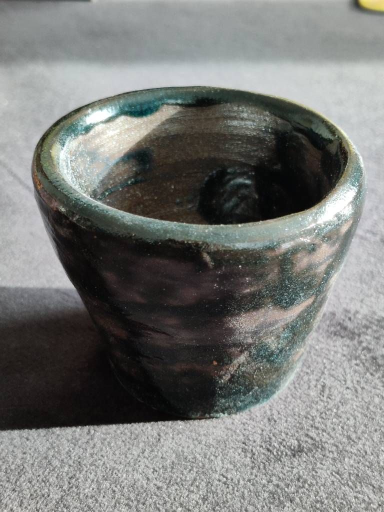 Pot en argile recouvert d'émail vert/noir (avec des reflets bleus sur la photo) posé de façon très irrégulière.