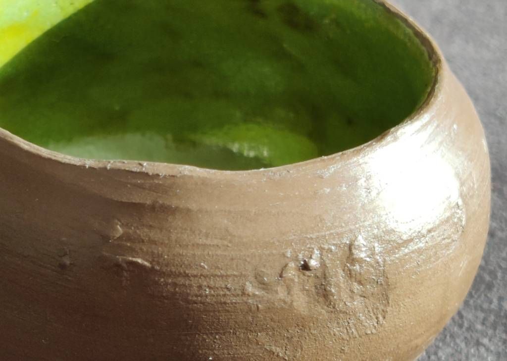 Détail en gros plan d'un pot en argile dont l'extérieur est laissé brut (argile marron, légèrement brillante car recouverte de cire) et intérieur vert anis.