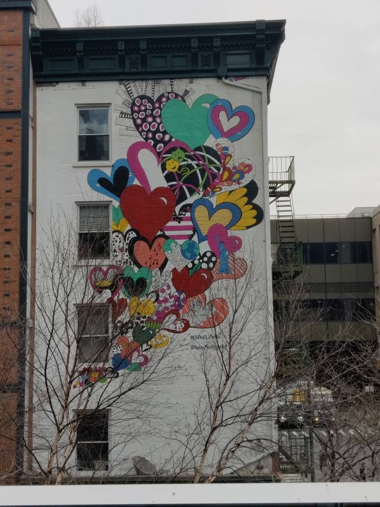 Graffiti s'étalant sur toute la façade d'un immeuble de trois étages représentant des cœurs de toutes les couleurs remplis de formes différentes s'envolant