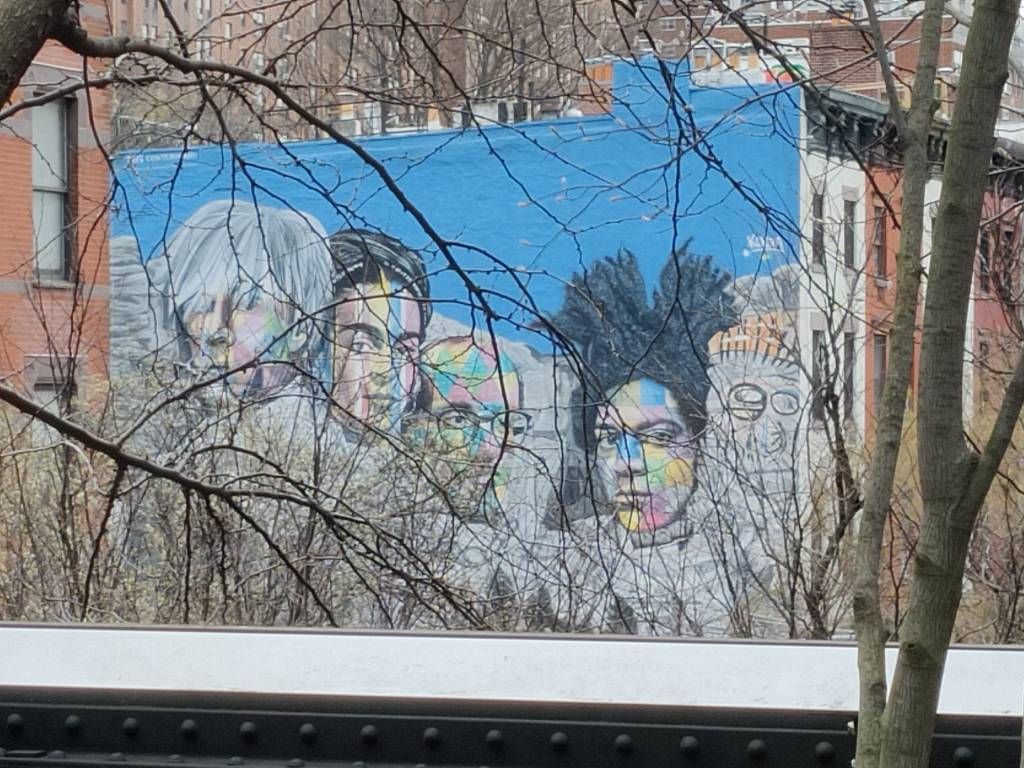 Graffiti partiellement caché par des branches reprenant le mont Rushmore mais avec les visage d'Andy Warhol, Frida Khalo, Kieth Haring et Jean-Michel Basquiat