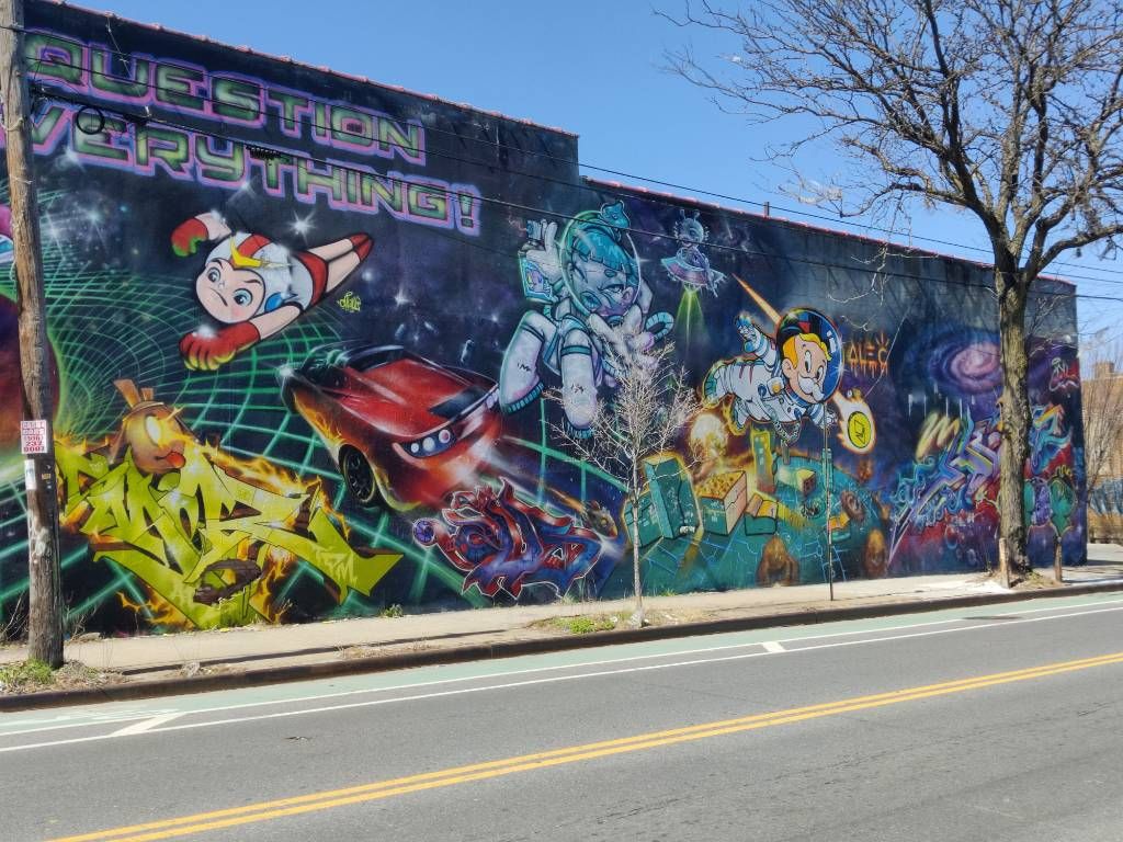 Graffiti style cartoon recouvrant un mur complet avec différents personnages liés à l'espace et sujets (voiture, ville, planètes...)
