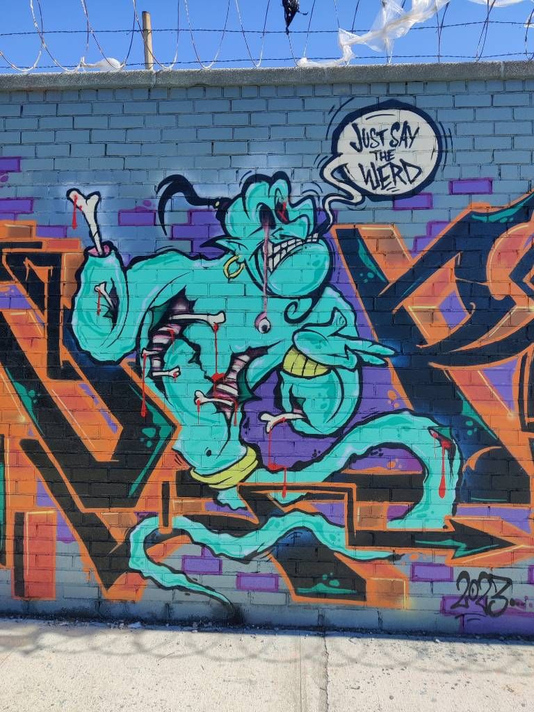 Détail d'un large graffiti qui reprenanait des personnages de Disney mais en en faisant des vampires, des monstres, etc. Ici, génie d'Aladin en zombie disant "Just say the werd"