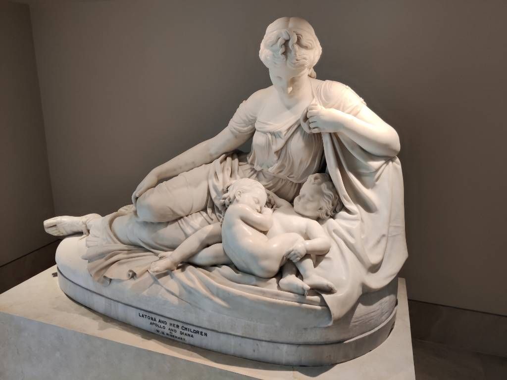 Sculpture en marbre blanc représentant une femme assise au sol avec deux jeunes enfants dormant appuyés sur elle et l'un sur l'autre
