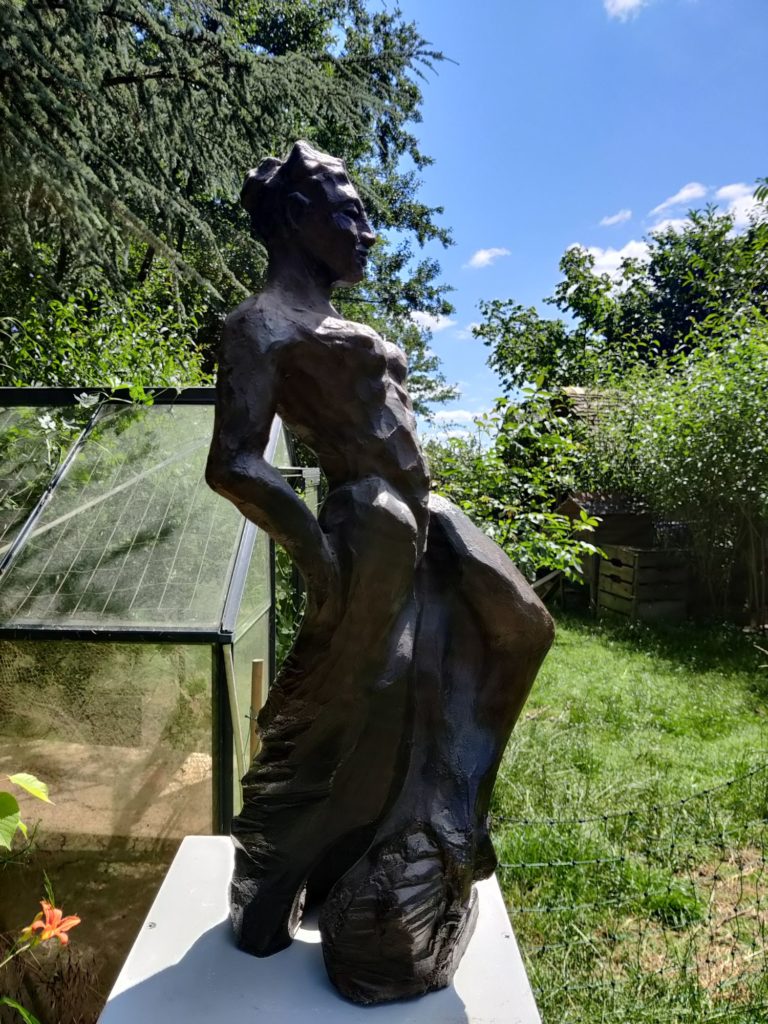 Une sculpture de femme vu de profil, le corps cambré, dans un jardin