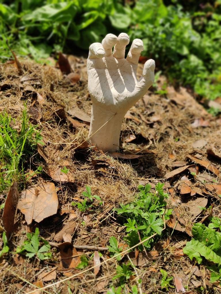 Sculpture d'une main qui a été posée à même le sol de sorte qu'on pense à un zombie essayant de sortir de terre