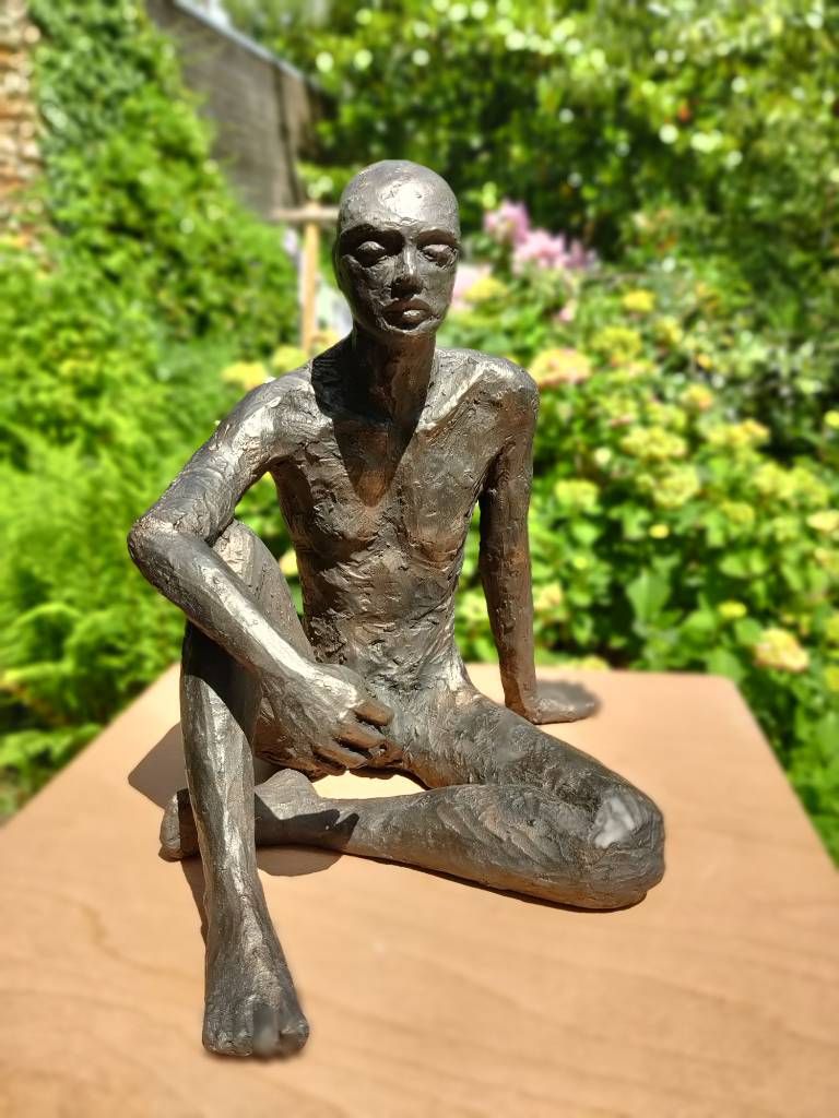 Sculpture qui a l'air d'être en bronze (c'est en fait une patine qui donne cet effet là) d'un homme assis, dans un jardin fleuri