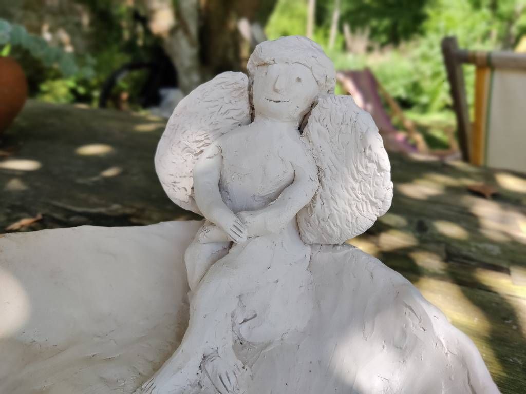 Sculpture au style naïf (elle a été faite par un enfant) représentant un ange assis, souriant